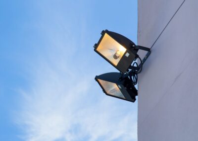 Two street lights on the side of a building against a blue sky.