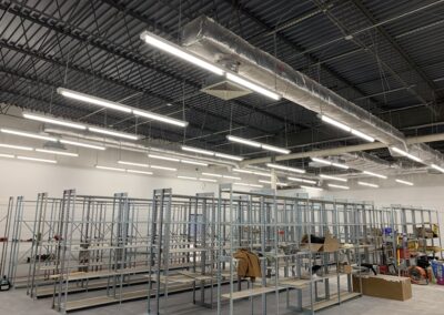 Interior of a warehouse with metal shelving units, ventilation ducts, and fluorescent lighting.