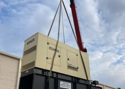 A large generator being lifted by a crane against a partly cloudy sky.