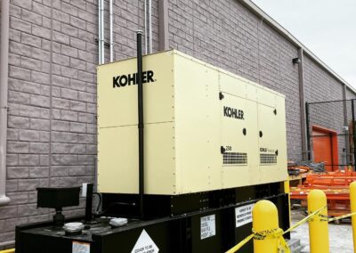 A kohler industrial generator installed beside a building with yellow safety bollards in the foreground.