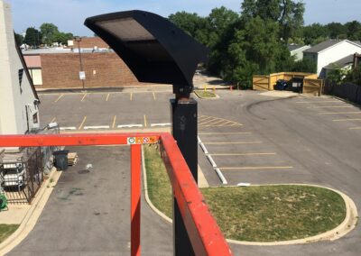 Solar panel installed on a pole overlooking an empty parking lot with buildings in the background.